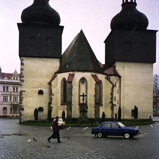 Historic church with classic architecture, cobblestone square, parked car, person crossing.
