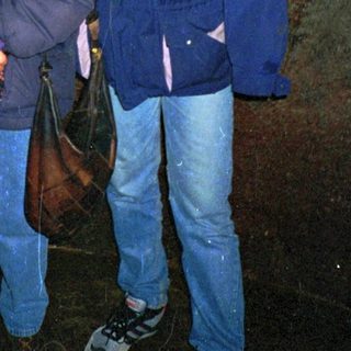 Two people standing indoors near a dark stone wall.