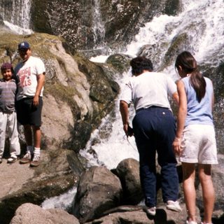 Family enjoying waterfall in natural rocky setting.