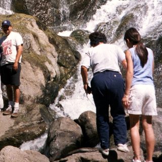 Family enjoying waterfall in natural rocky setting.