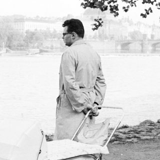 Man pushing a baby buggy near water.