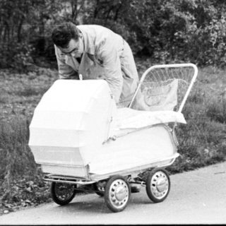 Man pushing empty stroller in park.