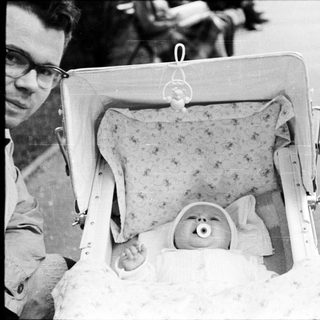 Man carries baby in open suitcase outdoors.