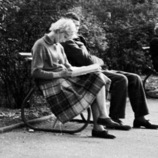 Man pushing stroller, sitting on bench outdoors.