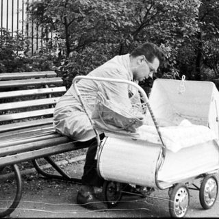 Man pushing stroller, sitting on bench outdoors.