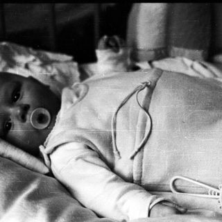 Infant with tracheostomy tube in hospital bed.