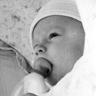 Newborn infant in incubator with "I love you" sign.