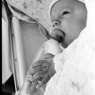 Newborn infant in incubator with "I love you" sign.