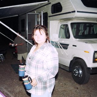 Woman standing near RV holding mugs.