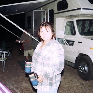 Woman standing near RV holding mugs.