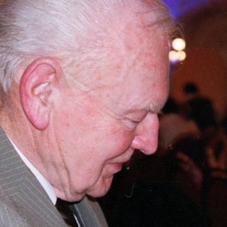 Elderly man drinking wine indoors at evening event.