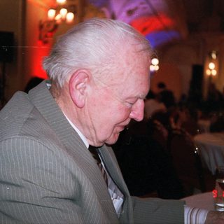 Elderly man drinking wine indoors at evening event.