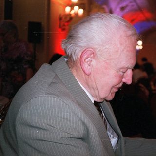 Elderly man drinking wine indoors at evening event.
