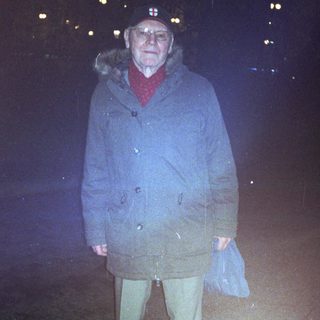 Older man wearing winter coat outdoors at night.