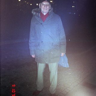 Older man wearing winter coat outdoors at night.