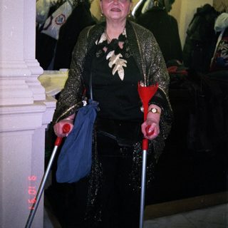 Elderly woman using canes indoors at event.