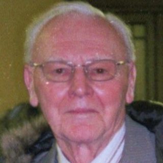 Elderly man in formal coat at indoor event.