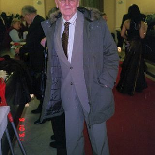 Elderly man in formal coat at indoor event.