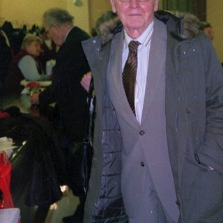 Elderly man in formal coat at indoor event.