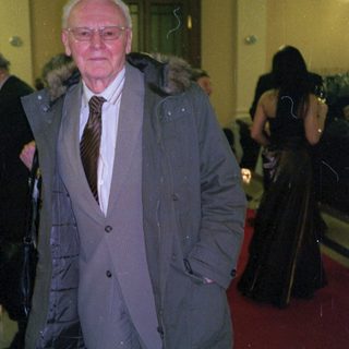 Elderly man in formal coat at indoor event.