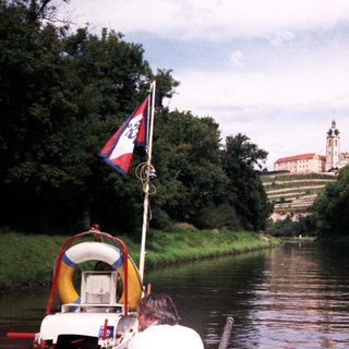 Scenic riverboat passing historic castle by water.