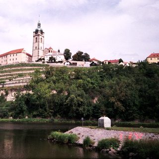 Historic castle complex by riverbank with vineyards.