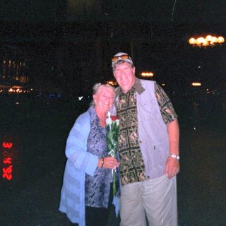 Two people posing together at night with lit city lights.