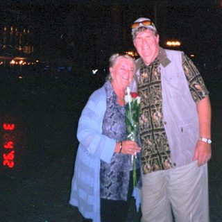 Two people posing together at night with lit city lights.