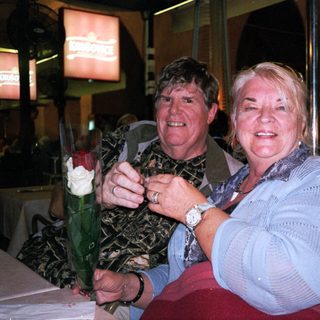 Two people smiling indoors holding a bouquet.