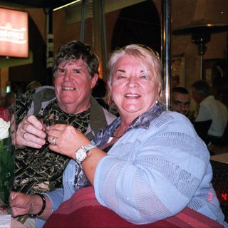 Two people smiling indoors holding a bouquet.