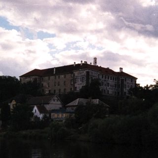 Large building on hill by calm river.