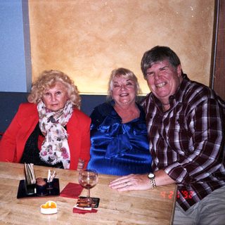Three adults smiling together indoors at a table.