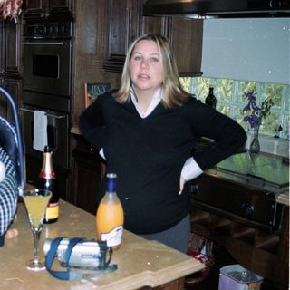 Newborn in carrier, woman standing by kitchen counter with drinks.