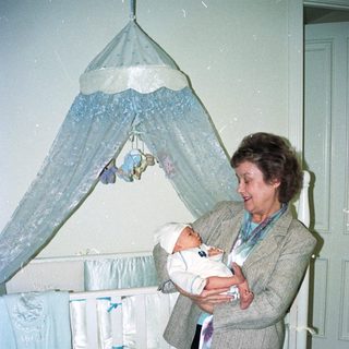 A woman holds a baby near a decorated crib.
