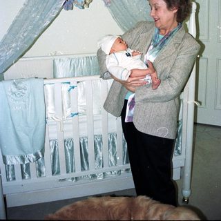 A woman holds a baby near a decorated crib.