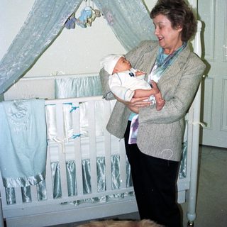 A woman holds a baby near a decorated crib.