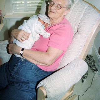 Elderly woman holding sleeping baby indoors.