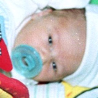 Baby sleeping in colorful playpen with cow-themed blanket.