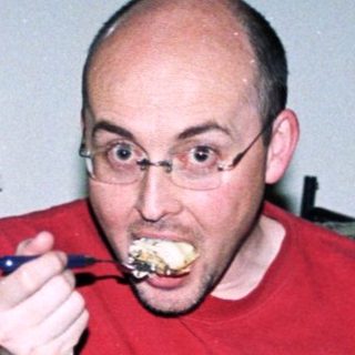 Man eating while holding baby on couch.