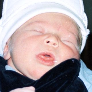 Baby wearing hat being held by adult.