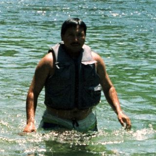 Adult supervises child playing in shallow river.