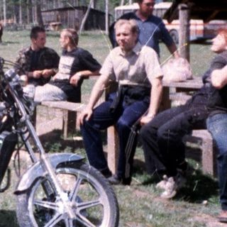 Two women posing on vintage motorcycle at outdoor gathering.