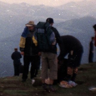 People hiking on mountain peak under cloudy sky.