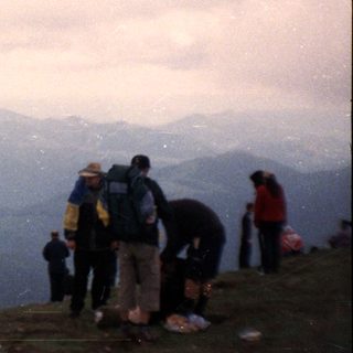 People hiking on mountain peak under cloudy sky.