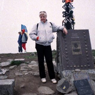 Person standing at summit plaque with hiking gear.
