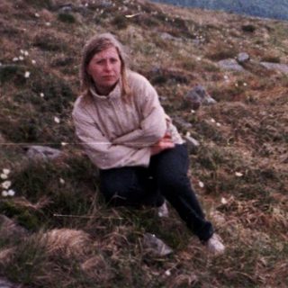 Person sitting on mountain peak overlooking valley.
