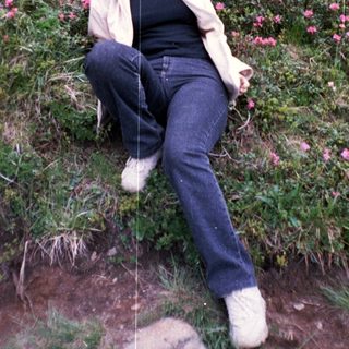 Woman sitting on grassy hillside with pink flowers.