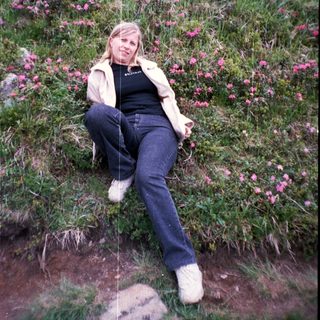 Woman sitting on grassy hillside with pink flowers.