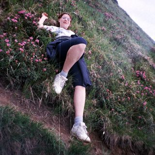 Person resting on grassy hillside near blooming flowers.