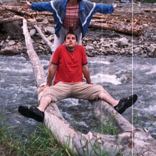 Two people sitting on fallen logs near a river.